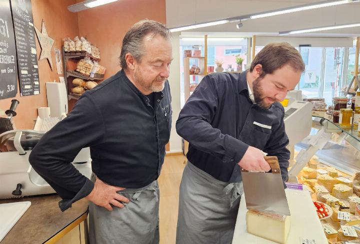 Rolf Gasser (l.) schaut «Lehrling» Andreas Meier über die Schulter, wie er Käse schneidet. Der Drogist musste zuerst eingearbeitet werden in diesem Fachgebiet. Umgekehrt erlebte Rolf Gasser dasselbe in der Drogerie. Fotos: mbe