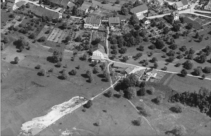 Das im Tiefflug aufgenommene Flugbild vom 20. Juni 1953 zeigt rechts der Bildmitte die Isolierbaustein-Fabrik auf dem Lochacker und die schnurgerade Rollbahn, mit der man den Kalktuff von der Lagerstätte in der Wey zur Fabrikationsstätte hochzog. Foto: Werner Friedli, ETH Bildarchiv (Ausschnitt LBS_H1_015037)