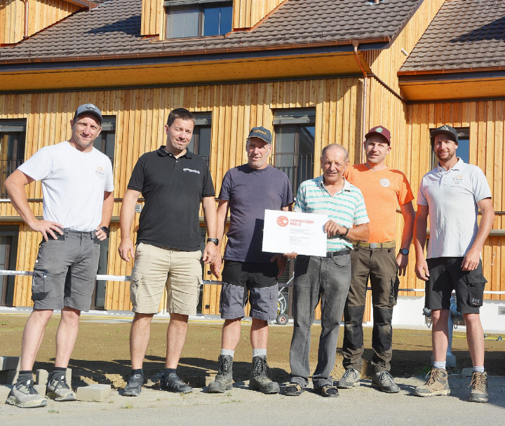 Stolz auf den Schweizer Holzpreis für das neue Mehrfamilienhaus hinter ihnen: (von links) Reto Saxer (R. Saxer Holzbau), Architekt Roman von Arx, Simon Kohler, Alois Kohler, Förster Guido Schibli und Roger Saxer (R. Saxer Holzbau). Foto: bba